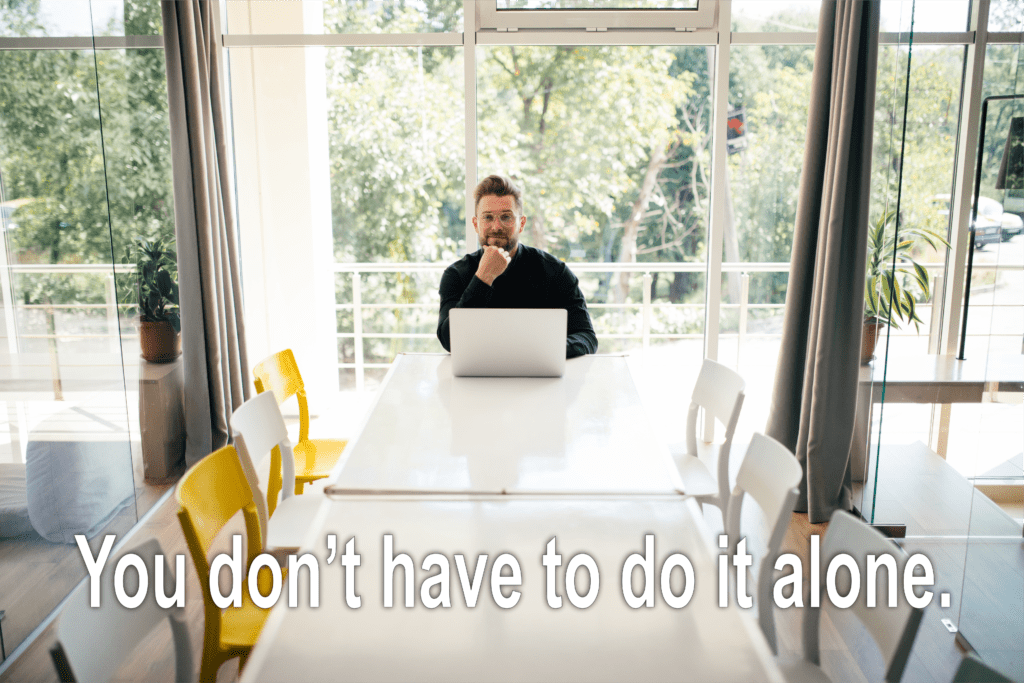 Man sitting at dining room table with laptop and chin on fist. Text overlay says You don't Have to do it alone.